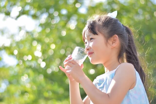 W-piatto　女の子が緑に囲まれながらコップに入った水をおいしそうに飲む写真